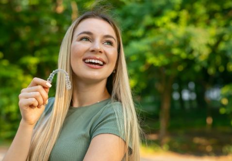 Smiling blonde woman holding a clear aligner