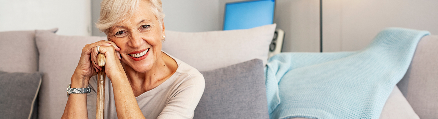 Smiling senior woman sitting on her couch and holding her cane